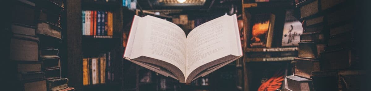 Glossar - A dark library with a book in a spotlight floating in the middle of the shelves.